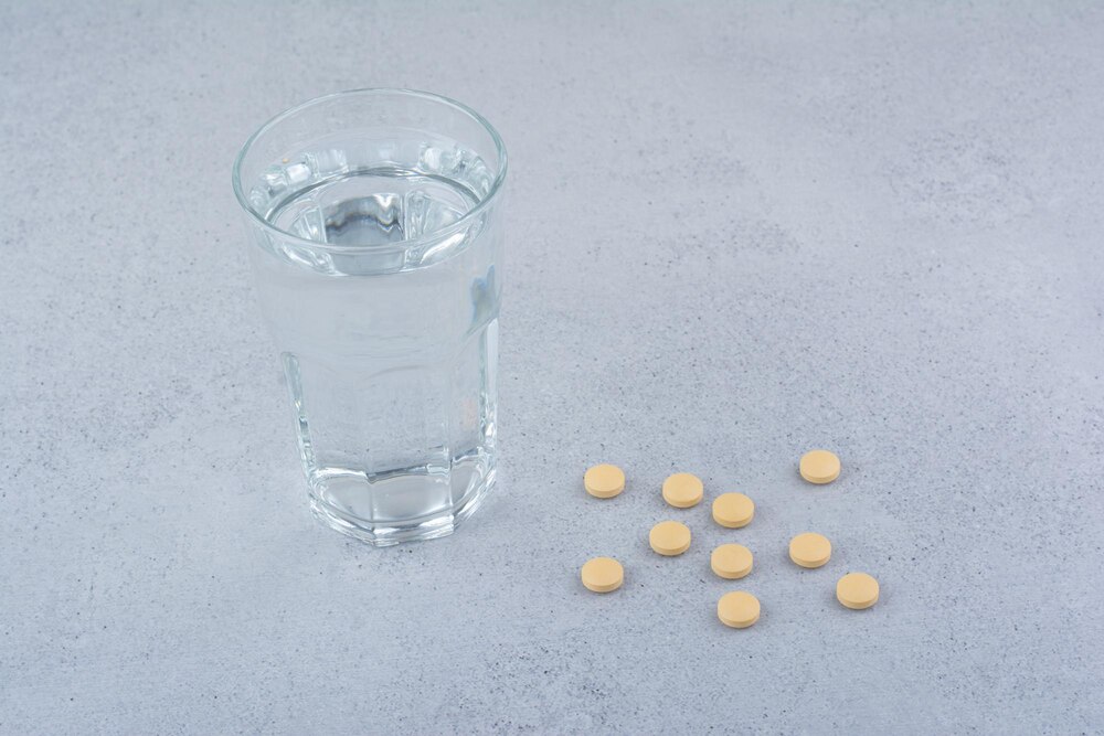 Two packs of red pills with glass of water.
